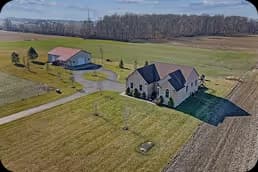 A large house with a dark roof and landscaped yard next to a detached garage on a spacious rural property