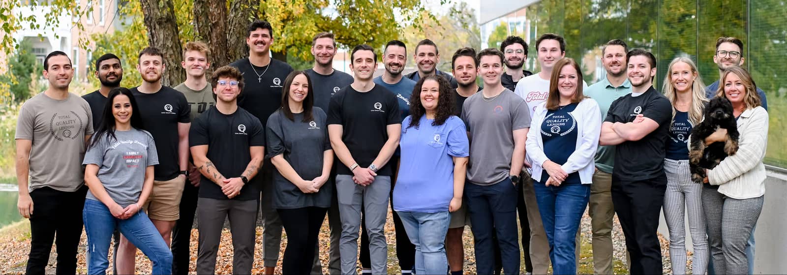 A diverse group of people standing outside on autumn leaves, smiling at the camera